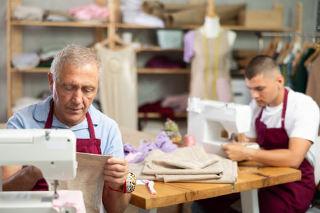 Elderly and young man sew on machine in workshopの写真素材