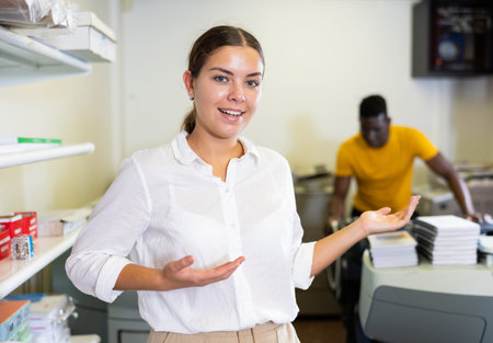 Happy young woman in white shirt sticking out her left hand to show the workflow in the printing...