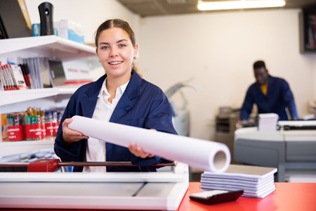 Happy young female specialist in a blue uniform holding whatman in a roll in the typography