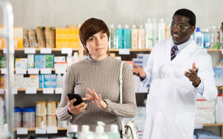 Woman with phone chooses medicines with help of pharmacistの写真素材