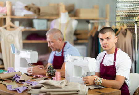 Elderly and young man sew on machine in workshopの写真素材