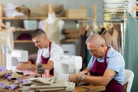 Elderly and young man sew on machine in workshopの写真素材