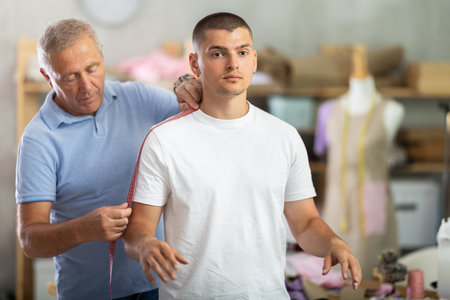 Elderly man tailor takes body measurements from young manの写真素材