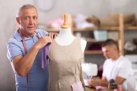 Elderly man working with mannequin, young man sewingの写真素材