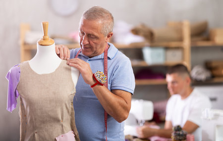 Elderly man working with mannequin, young man sewing