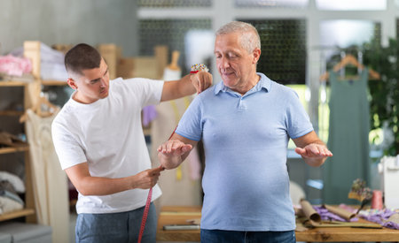 Young Tailor Taking Measurements From Elderly Manの写真素材