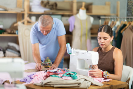 Young woman sewing, male assistant attaching template to fabricの写真素材