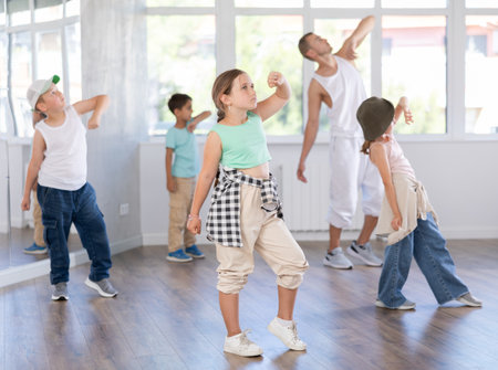 Positive cheerful smiling children studying modern style dance in class indoors with male teacherの写真素材