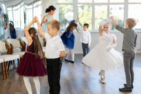 Little children in elegant dresses practicing waltz dance in school hallの写真素材