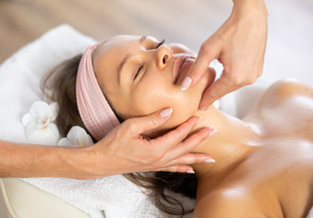 Young woman enjoying professional massage of neck, collarbone and chestの写真素材