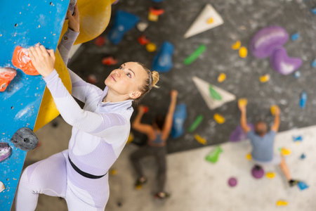 Concentrated woman moving up bouldering wall in climbing gymの写真素材