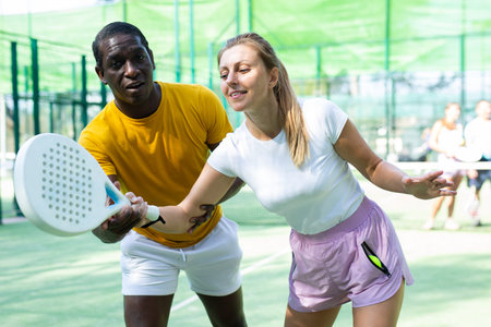 Portrait of concentrated african american trainer teaching woman playing padel outdoor