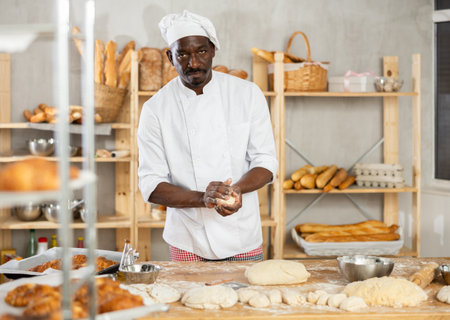 Skilled black baker handling dough portions in artisan bakeryの写真素材