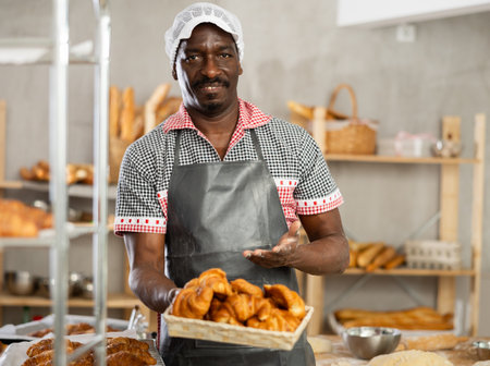 Smiling African baker offering freshly baked croissants in bakeryの写真素材
