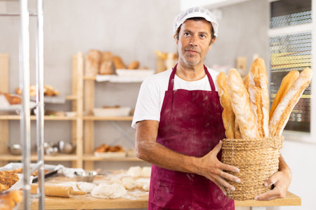 Caucasian male cook-baker worker with basket of baguettes, shows many products