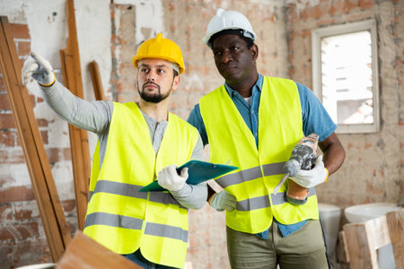 Two builders discussing working plan in apartment during repair works