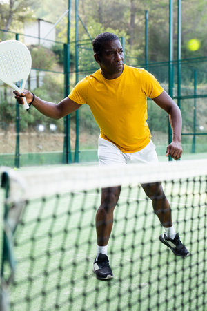 African american male player ready to hits the ball while playing padel on hard courtの写真素材