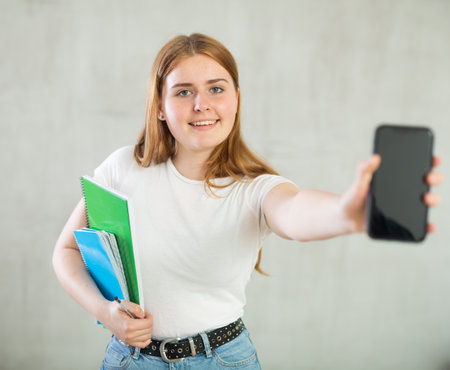 Young girl student showing modern smart phone with blank screenの写真素材