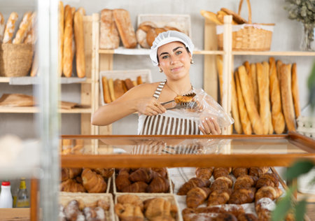 Young female seller putting croissant in bag