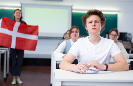 High school teacher tells students about Denmark and holds a Denmark flag in hands.の写真素材