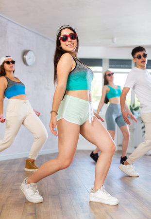 Group of young girls in dark glasses and ball cap and guy dance shuffle in fitness club