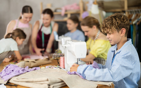 Boy learns to sew on sewing machine in class as children watch himの写真素材