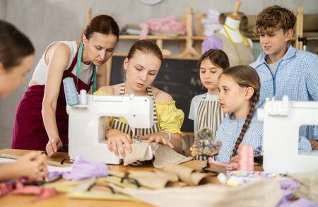 Schoolgirl practicing stitching at machine under guidance of instructor at lessonの写真素材