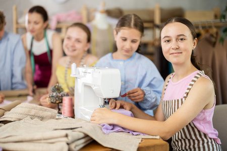 Teenage girl works on sewing machine while teacher and children learn how to cut fabricの写真素材