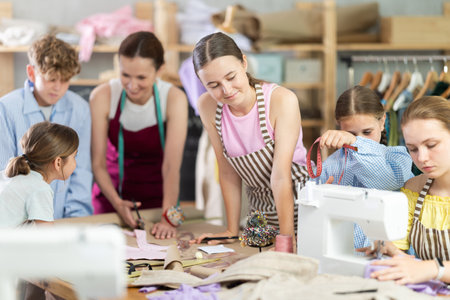 Teen girl watching peer sewing at machine during classの写真素材