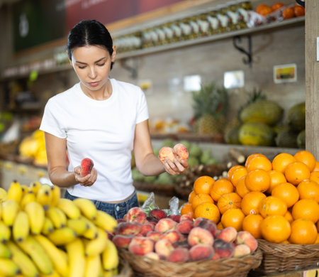 Focused woman shopping in organic food store, choosing flat peachesの写真素材