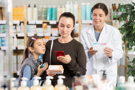 Middle-aged woman with daughter scanning barcode on pills in drugstoreの写真素材
