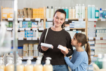 Woman with daughter choosing pills in pharmacyの写真素材