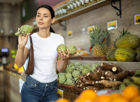 Girl client near vegetable stand in store choose artichokeの写真素材