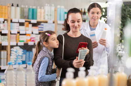 Woman with daughter scanning barcode on skincare lotion to check ingredientの写真素材