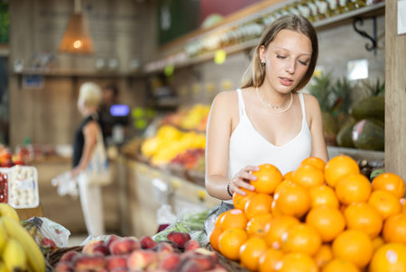 Woman near vegetable stand in store choose orangeの写真素材
