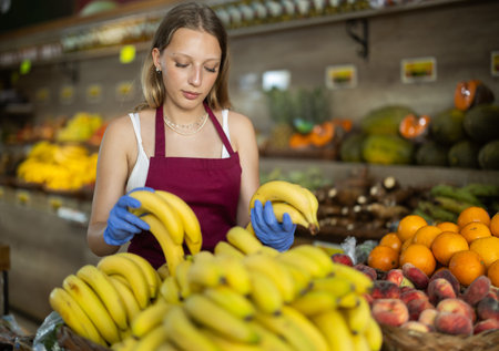 Girl shop seller add banana goods on display case in vegetable storeの写真素材