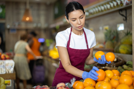 Adult female seller putting oranges in vegetable shopの写真素材