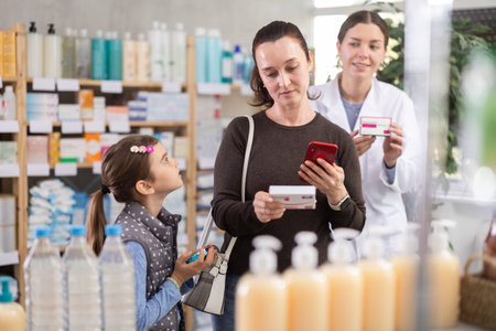 Woman with a child scans a package of pills against the background of a pharmacistの写真素材