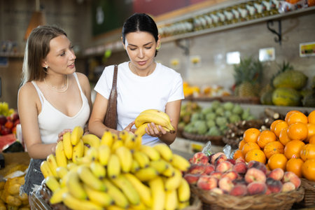 Two women are standing near the counter and choosing bananasの写真素材