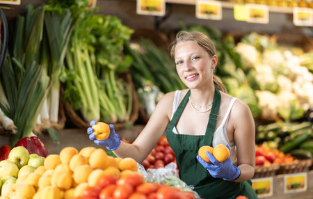Working in supermarket - female salesman sorts through ripe peaches on display caseの写真素材