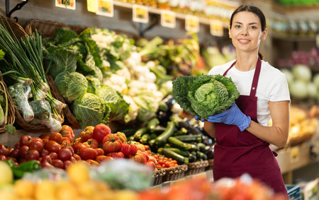 Female grocery store worker offers ripe broccoli cabbage in grocery department of supermarketの写真素材