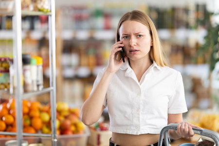 Angry young woman choosing groceries while talking on phoneの写真素材