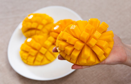 On plate - parts of cut ripe mango. Female hand holds one half of orange mangoの写真素材