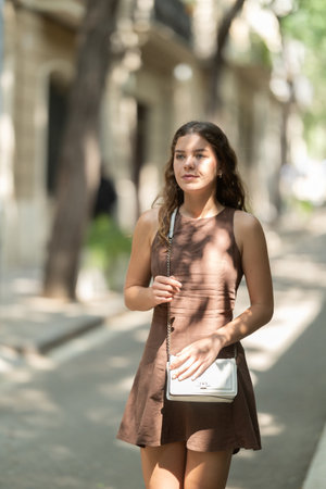 Beautiful smiling young lady wearing short dress walking shady tree lined street and relax in summer weather with sunshine outdoorの写真素材