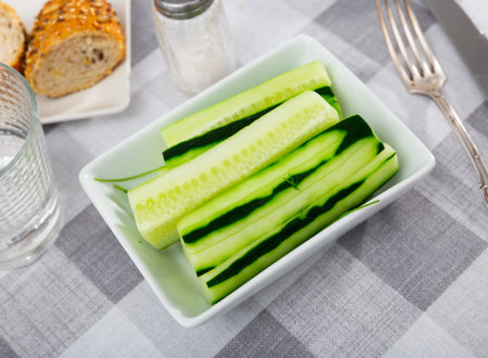 Peeled sticks long pieces of juicy cucumber pulp are laid out on plate. Vegetable snack, vegan side dish, decorated by dillの写真素材