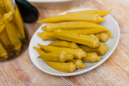 Pickled okra pods on plate on wooden table, homemade preservesの写真素材