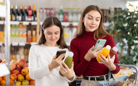 Teenage girl and her mother scanning QR on bottle of smoothie in supermarket. High quality photoのeditorial素材