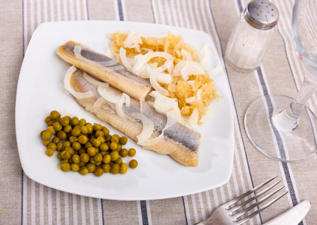 Light salted herring with pickled cabbage and green peas dished up in a plate on the laid tableの写真素材