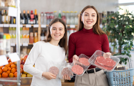Teenage girl and her mother choosing hamburger or beef entrecote in groceryの写真素材