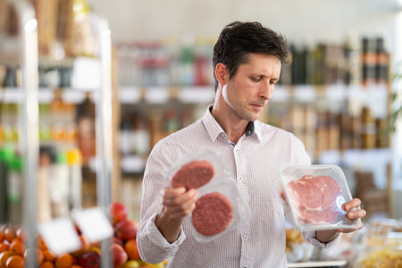 Man in light shirt choose and buy raw cooled beef entrecote and hamburger cutlet in storeの写真素材
